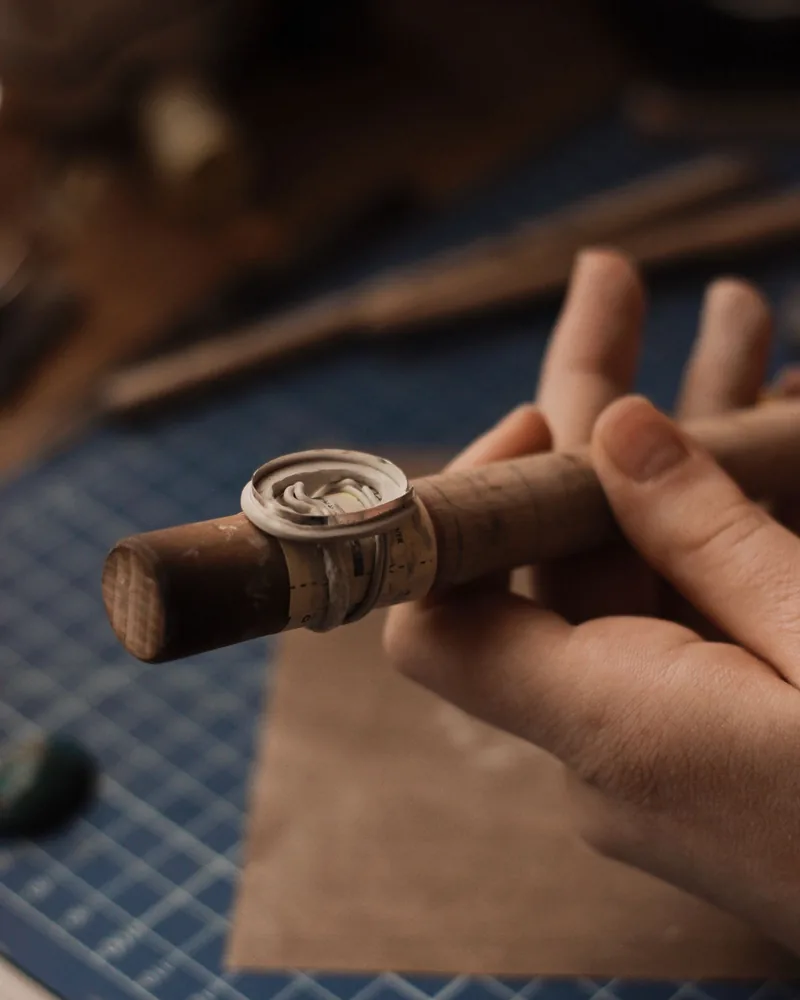 Detalle de las manos de un artesano sujetando con pinzas un anillo de plata durante el trabajo en el banco